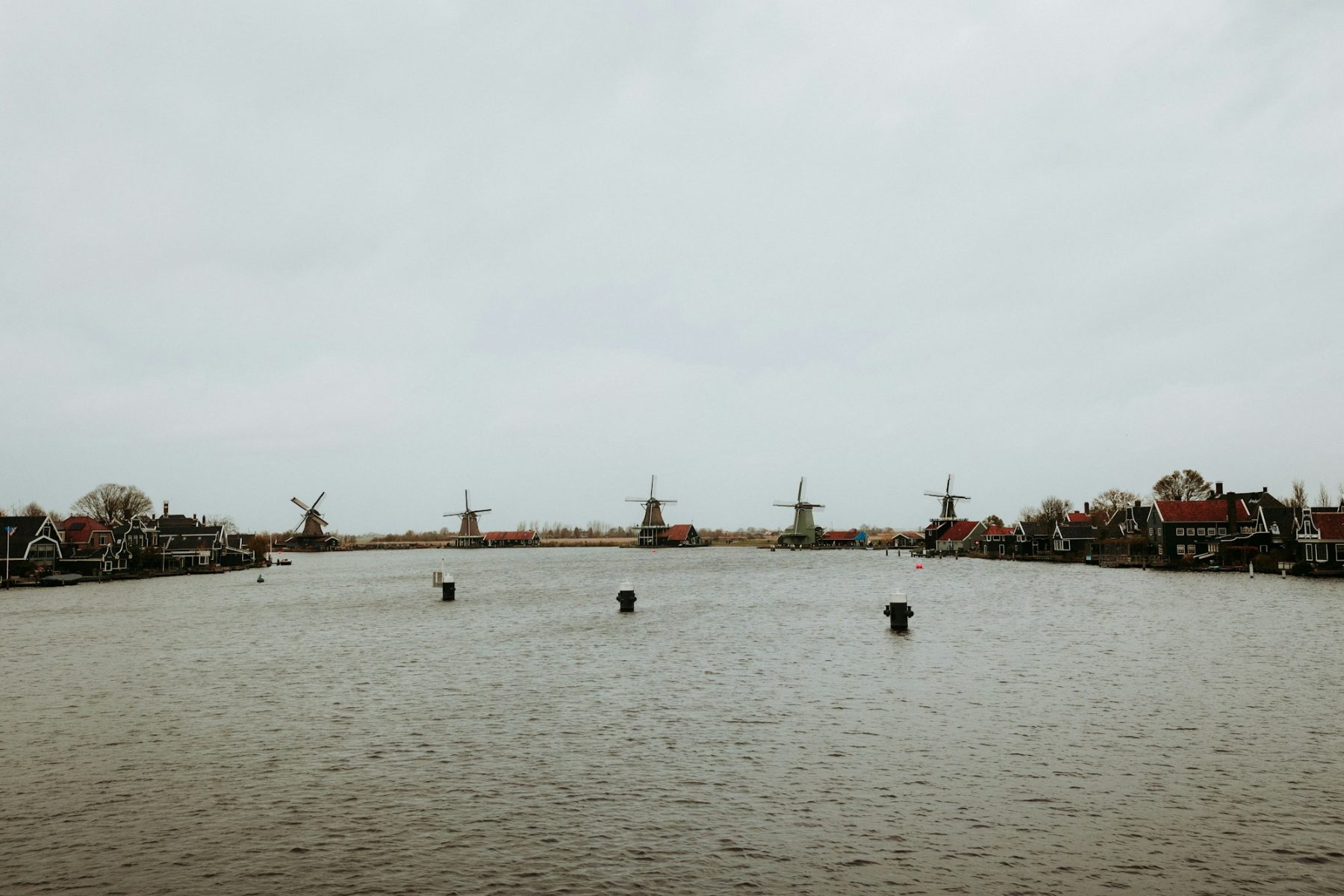 Breed grijs water met een lage Zaanse skyline onder een bewolkte lucht.